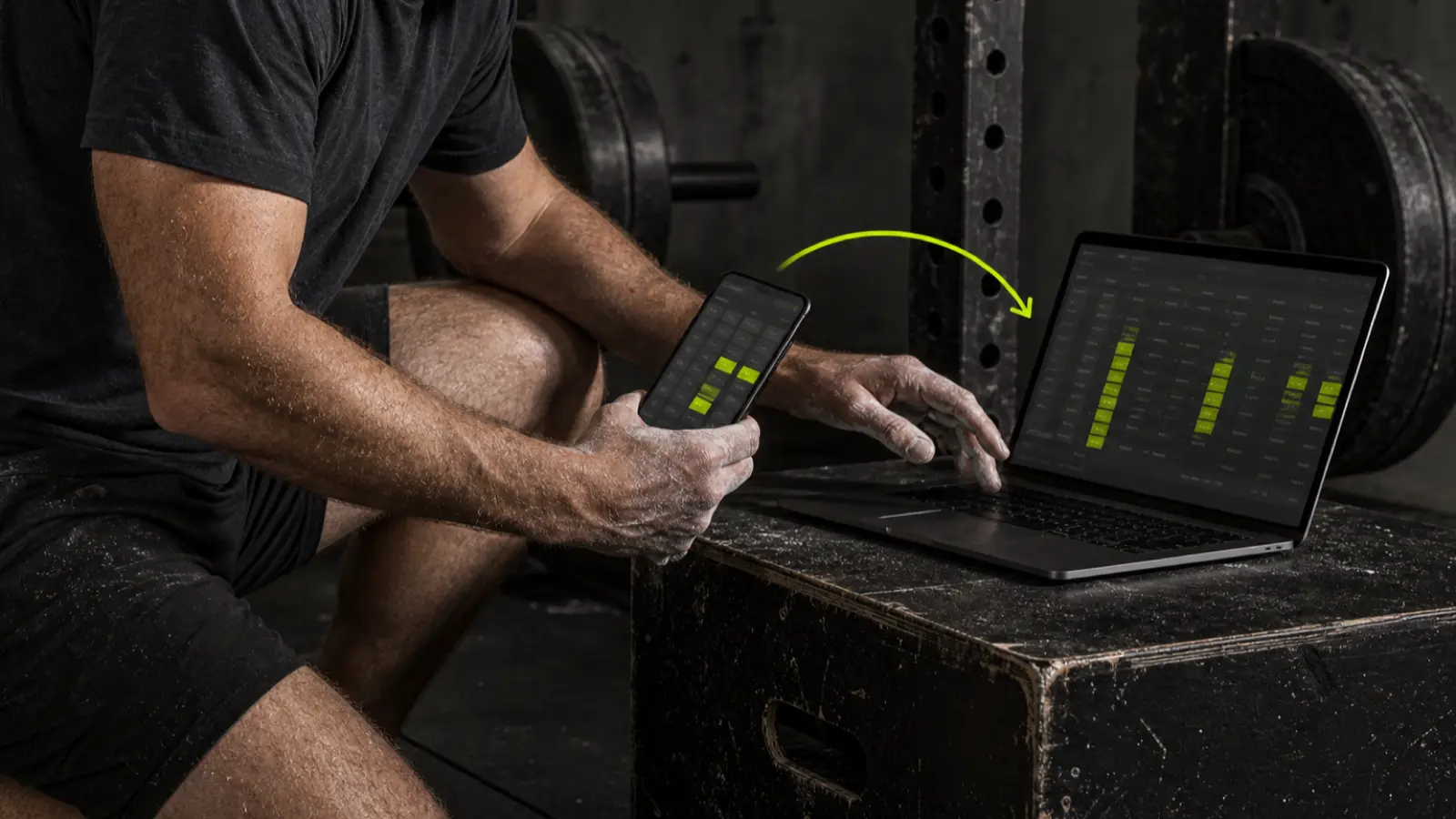 A lifter exports workout history from a phone into a laptop spreadsheet in a dark gym