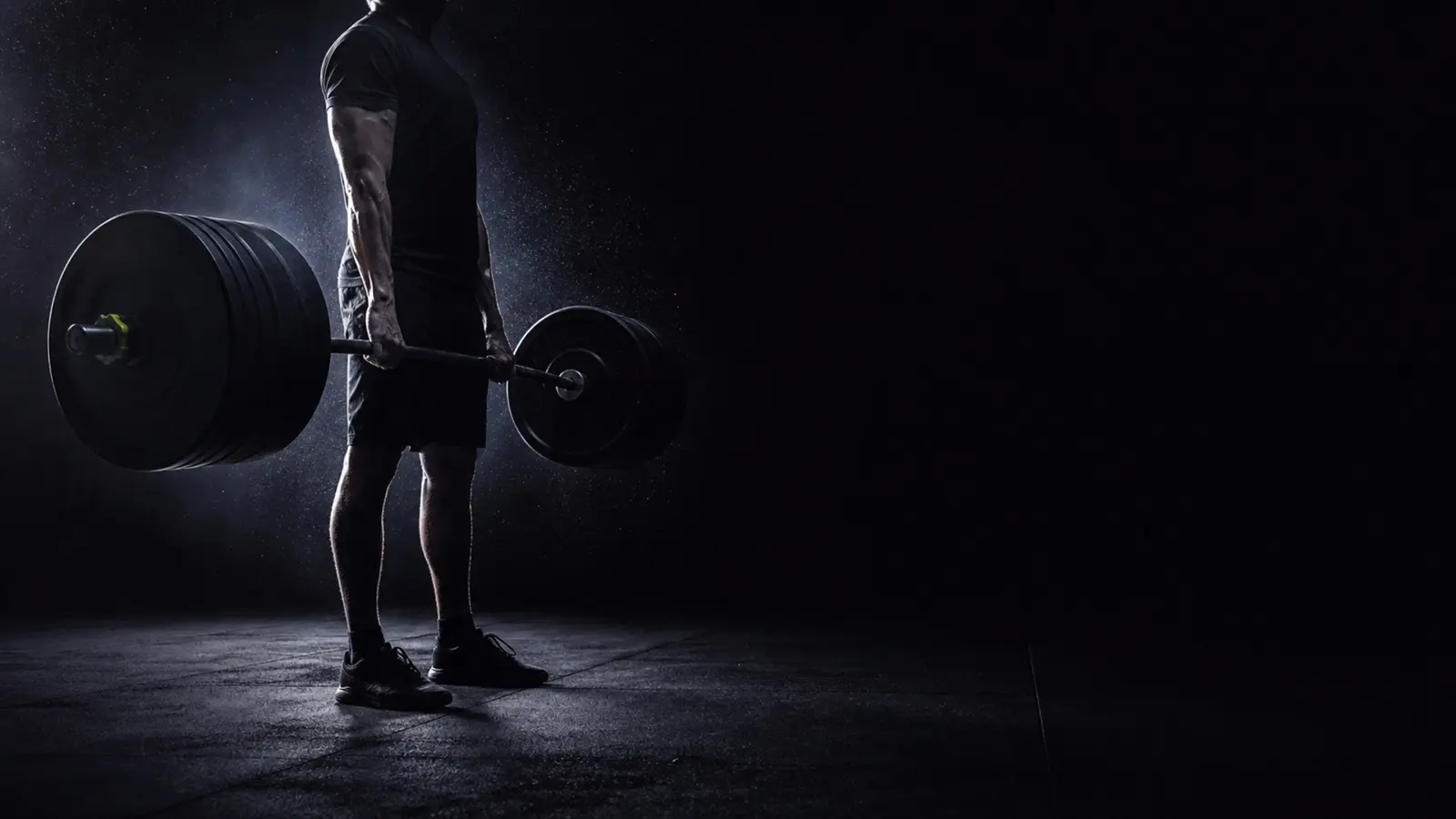 Lifter locking out a heavy deadlift in a dark gym, chalk dust in the light