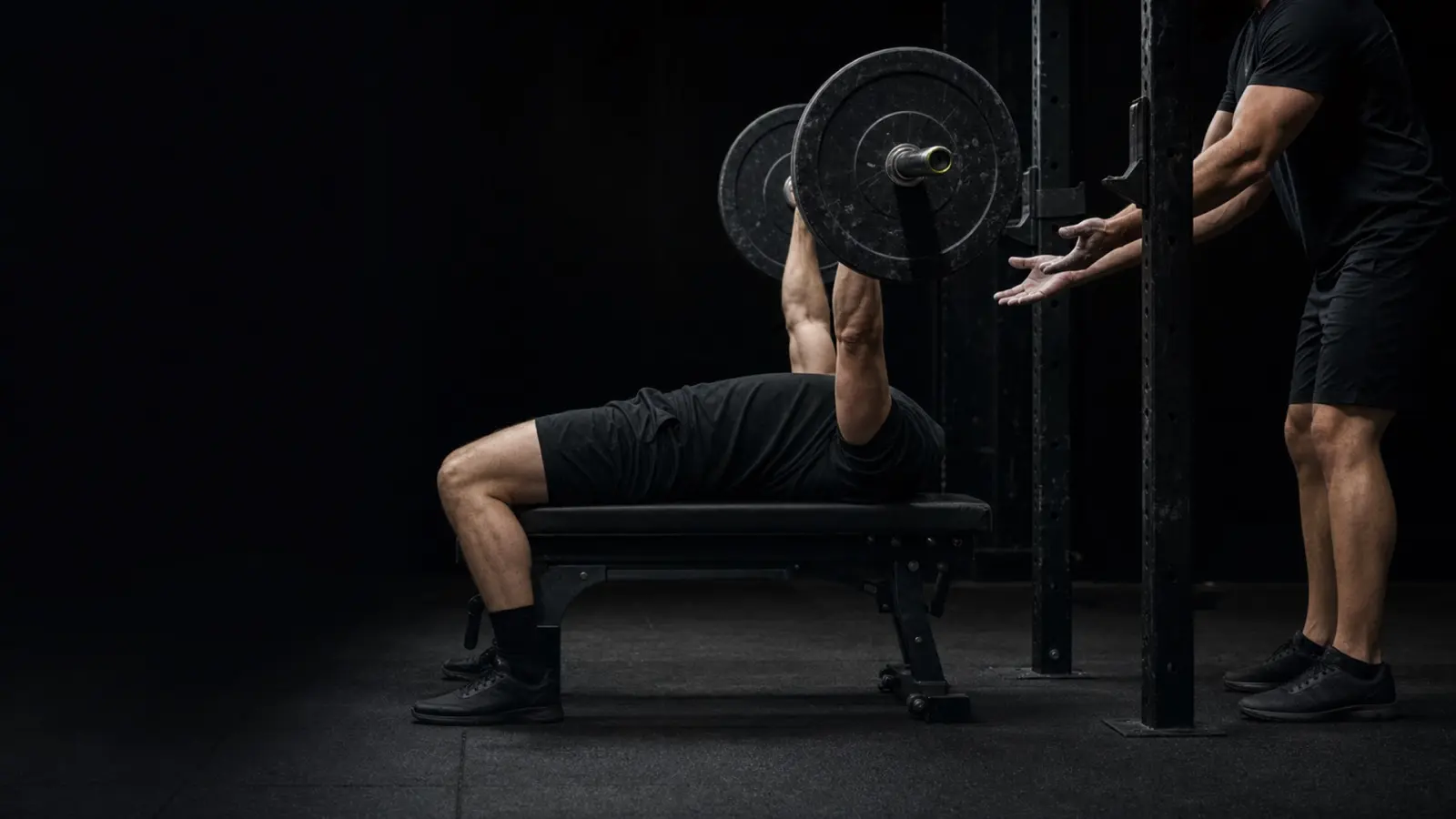 Spotter's hands hovering under the bar during a heavy bench press attempt